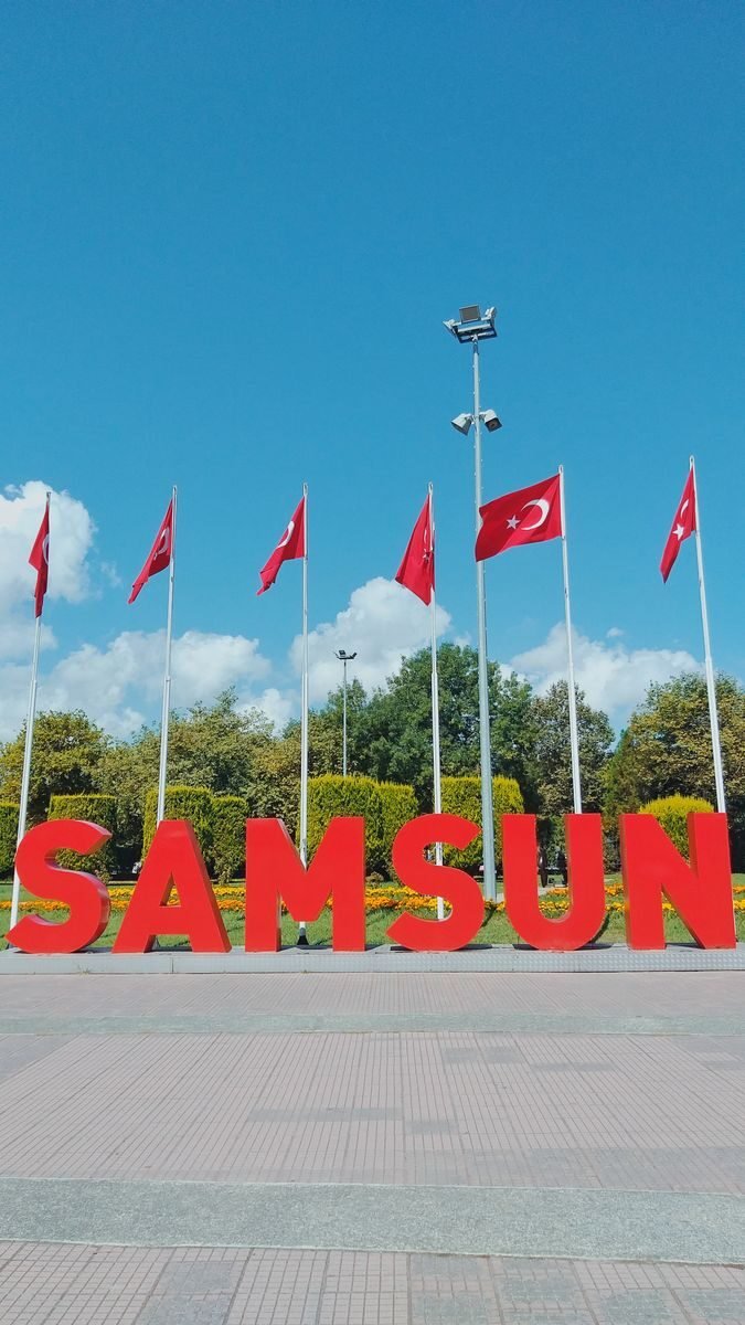 Colorful Samsun city sign with waving Turkish flags in a bright, sunny setting, showcasing regional pride.