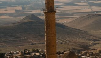 Scenic view of a historic minaret in Mardin, Türkiye, with vast plains and mountains in the background.