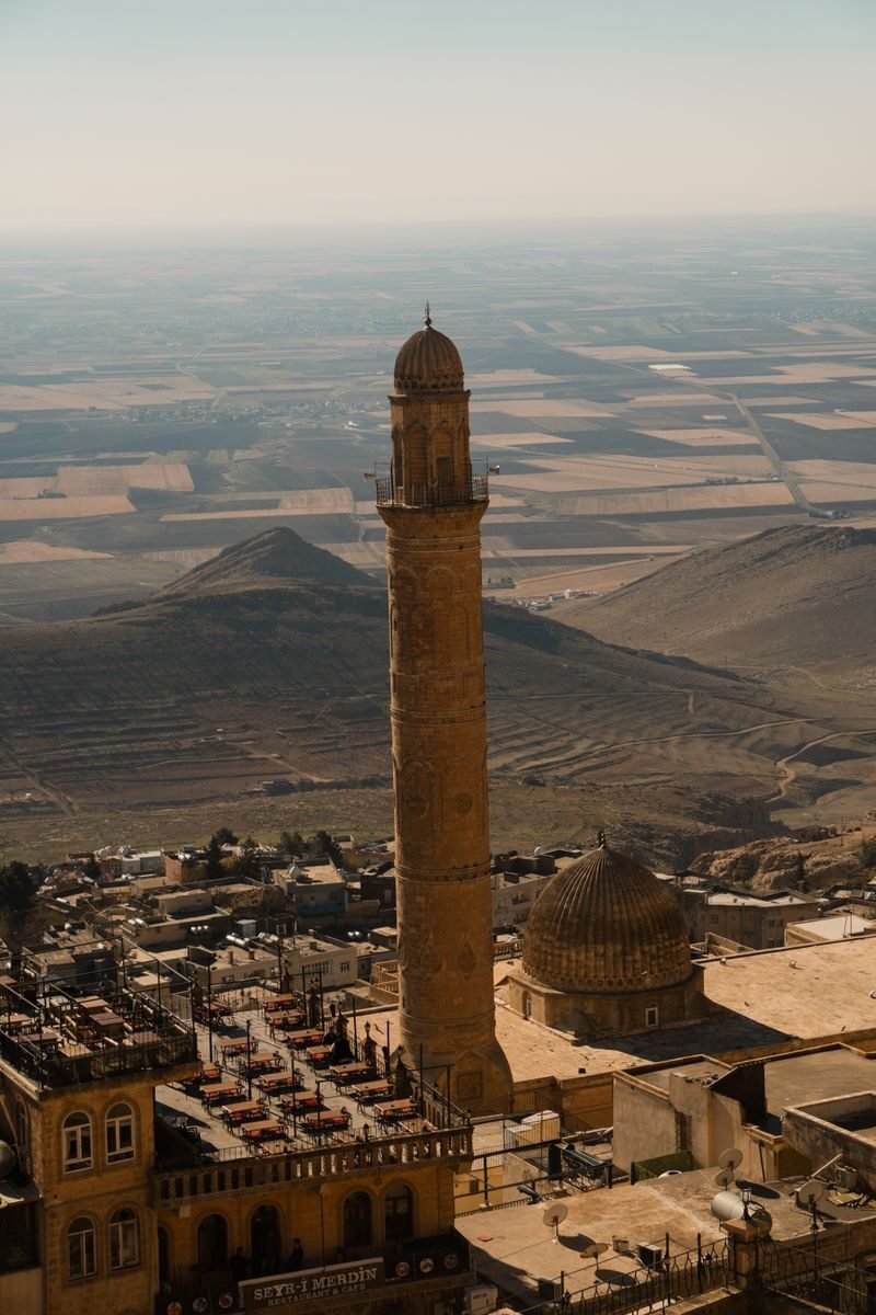 Scenic view of a historic minaret in Mardin, Türkiye, with vast plains and mountains in the background.