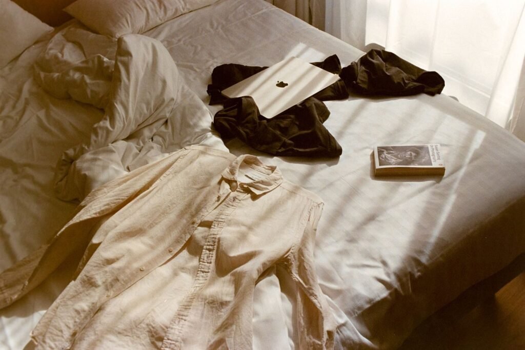 A relaxed bedroom scene featuring clothes, a book, and a tablet on a bed.