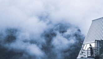 A solitary figure observes a fog-covered mountain landscape from a balcony, capturing a serene and introspective moment.