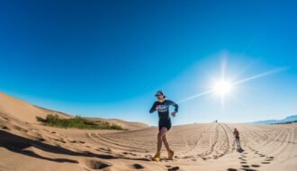 A runner in vibrant attire dashes across the sunlit desert dunes under a clear blue sky.