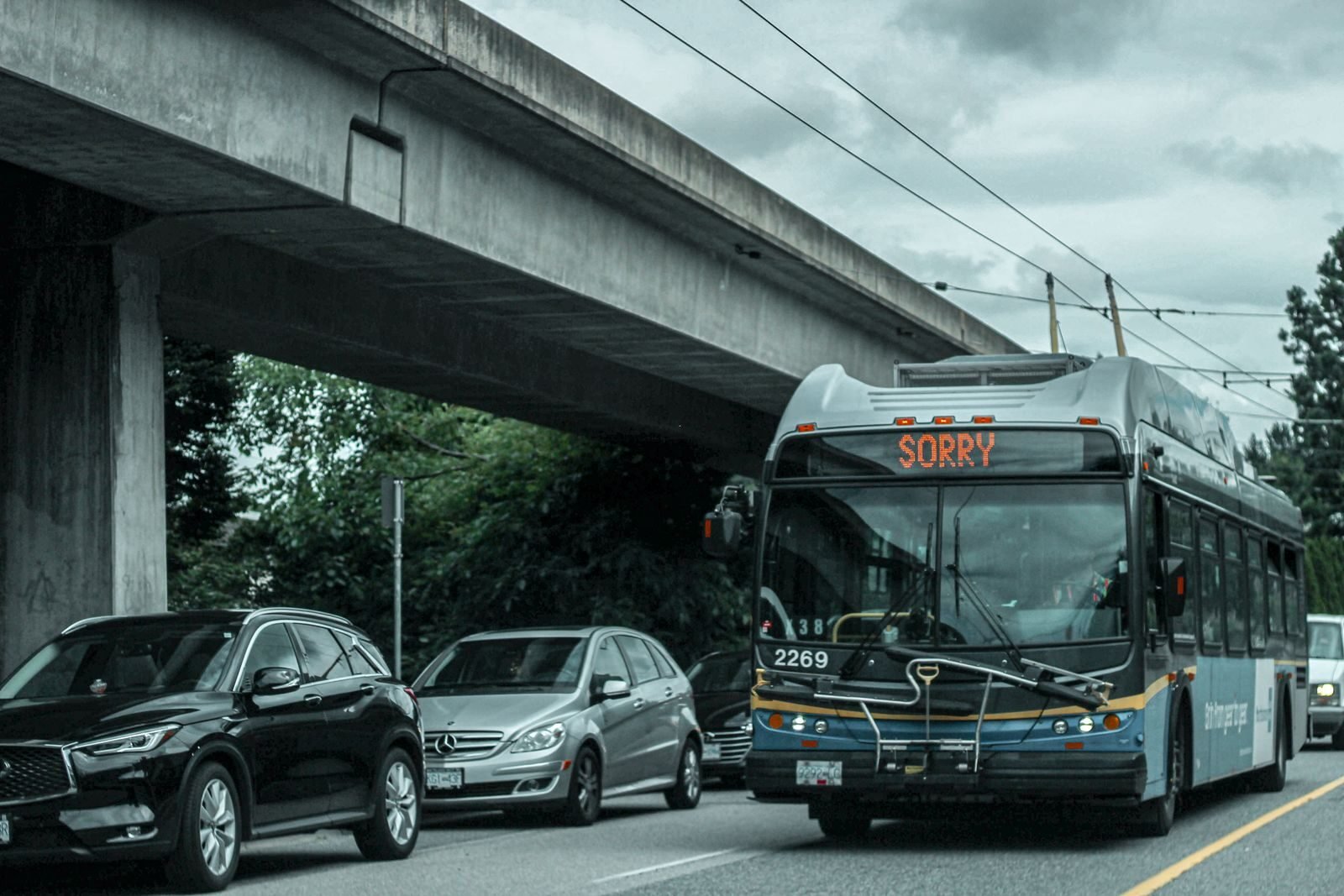 A busy city street with traffic and a bus showing 'SORRY' on its display under an overpass.