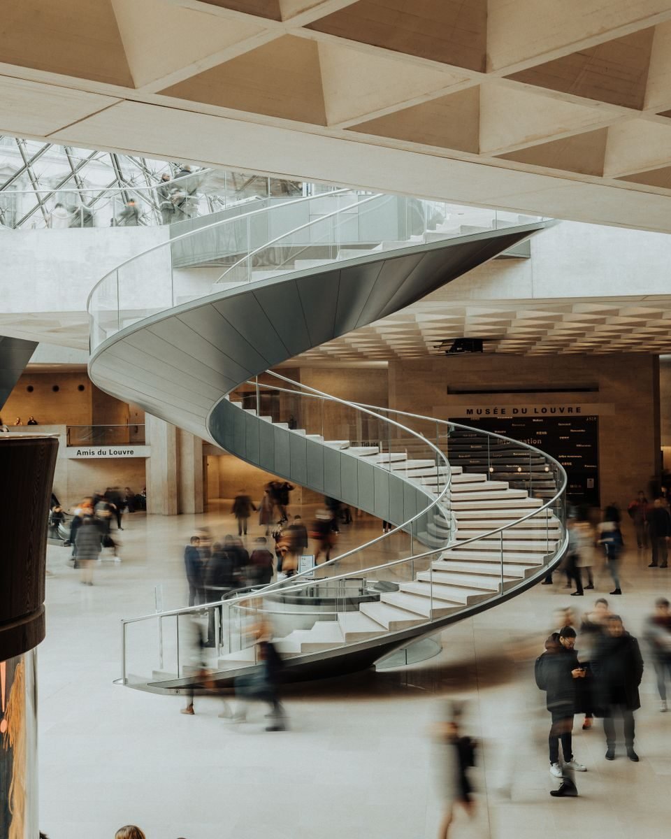 Visitors explore the modern spiral staircase in the Louvre's main hall in Paris.