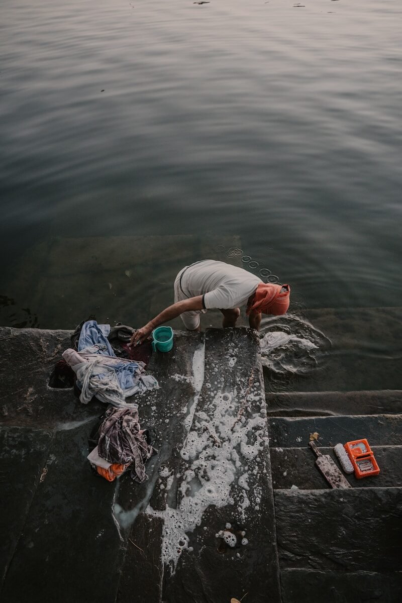A person washing clothes in the water on stone steps.
