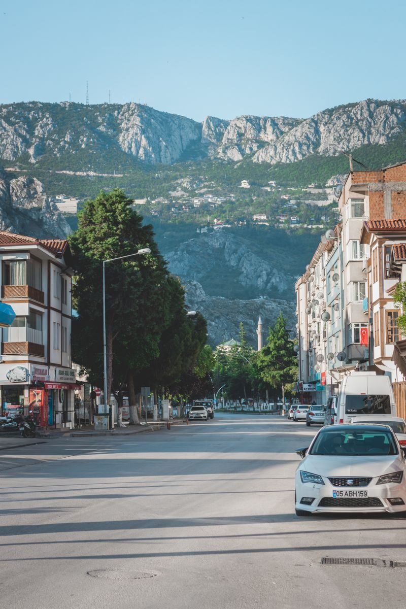 A quiet urban street lined with cars and buildings, set against a majestic mountain backdrop under a clear sky.