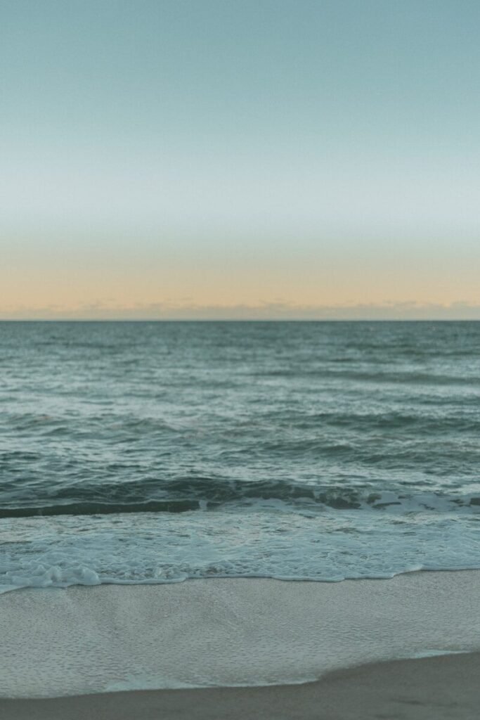 Gentle waves lap onto a sandy beach at dawn.