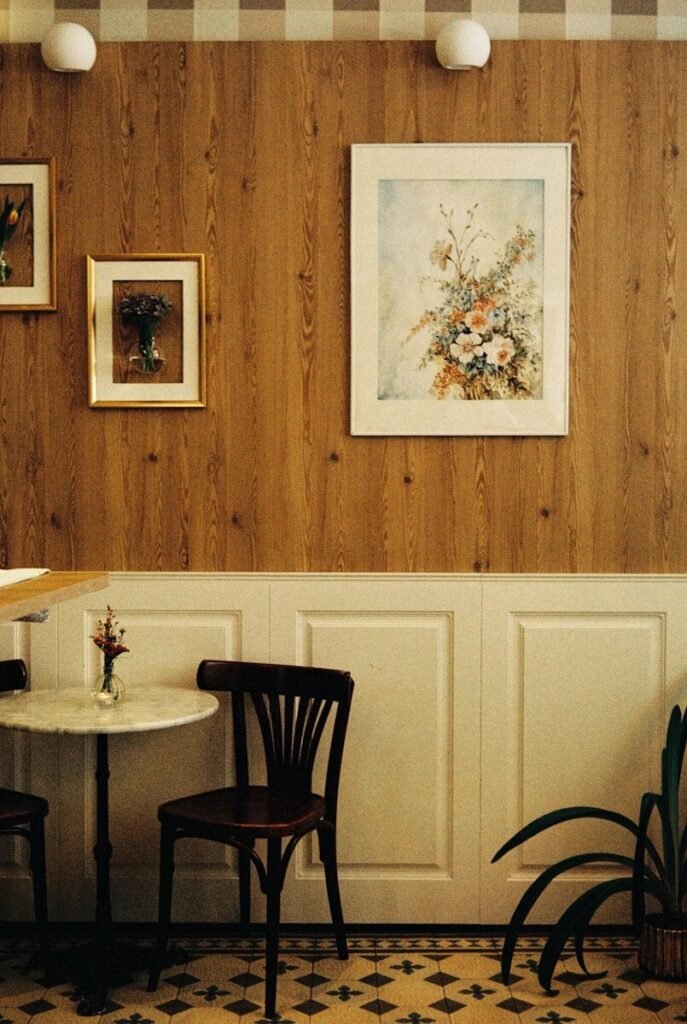 Cozy cafe interior with wooden walls, floral art, and table.